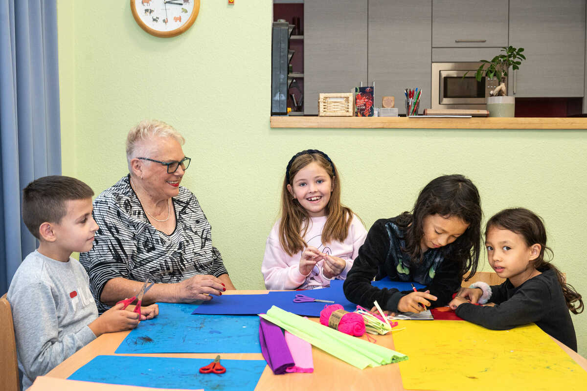 Eine Ehrenamtliche sitzt mit Kindern am Tisch und bastelt mit Wolle.